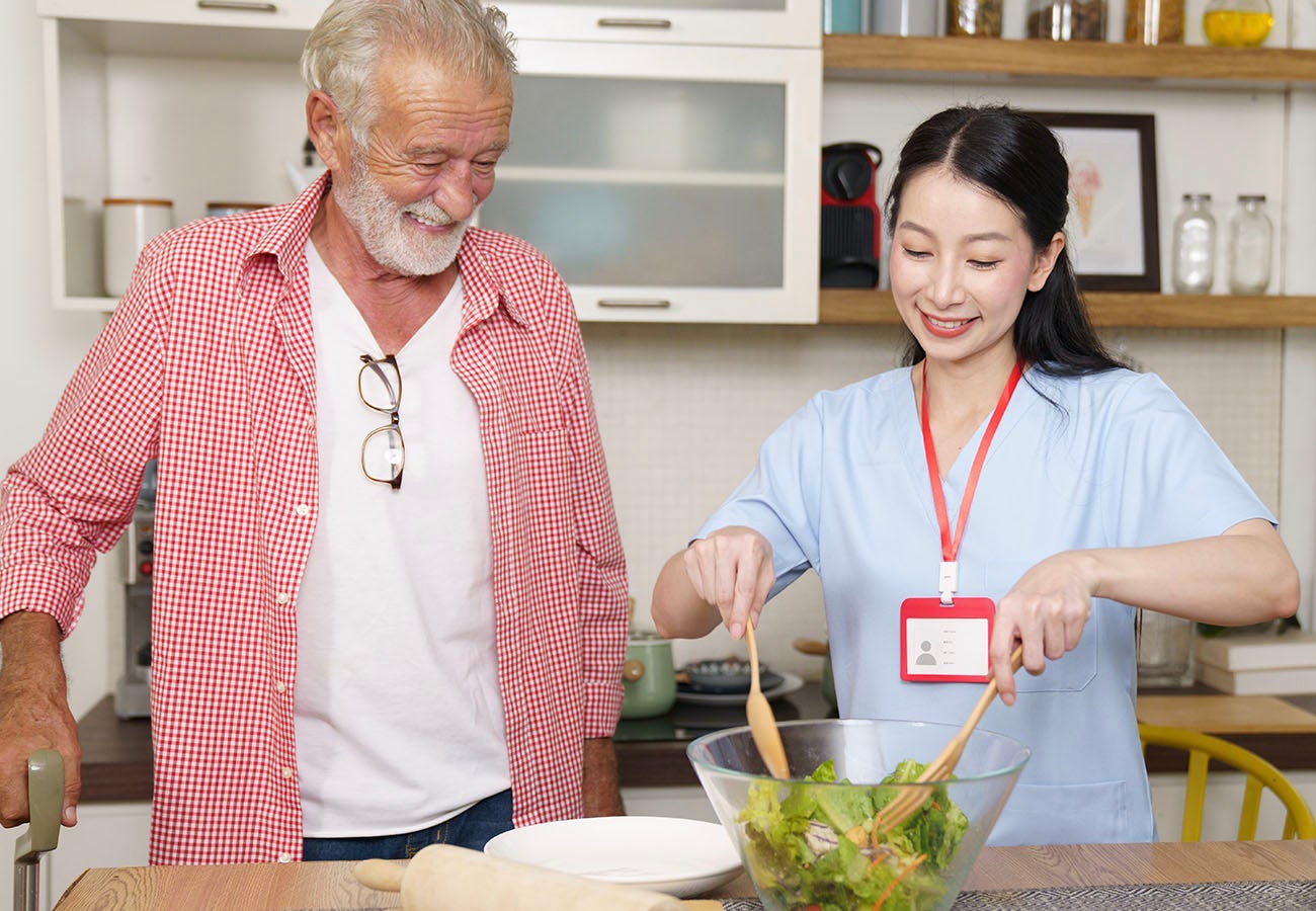 Female caregiver who was screened using GenAI solution helping elderly man prepare dinner in his home