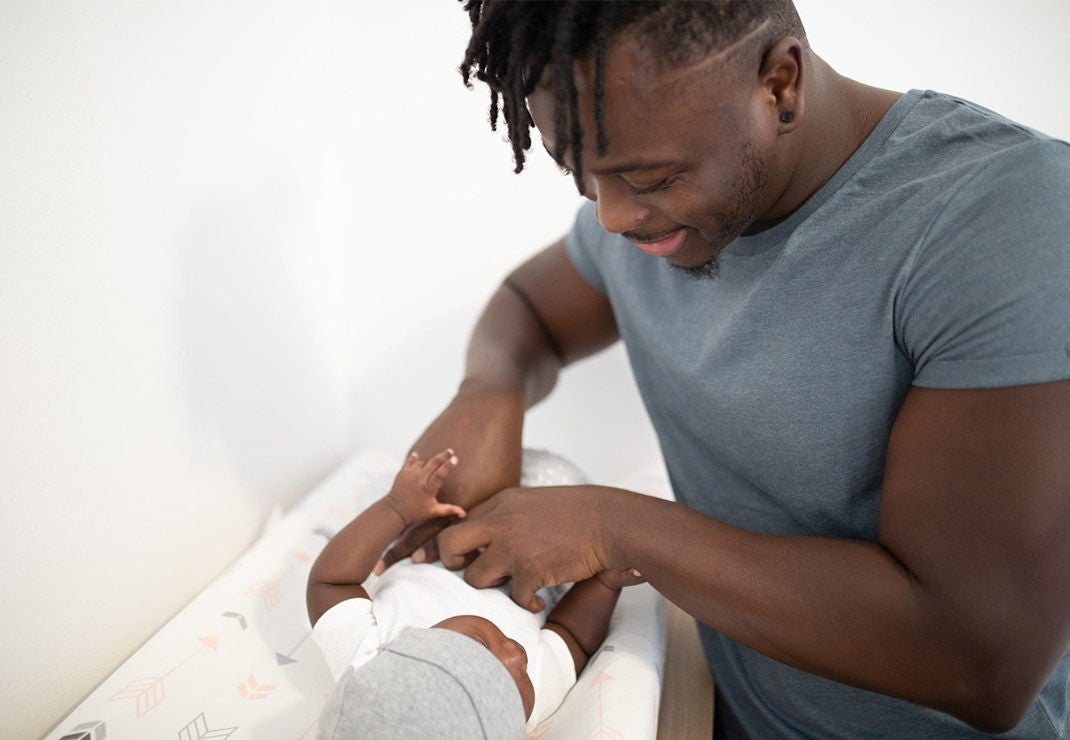 Father looking down at his baby as he is changing his clothes.