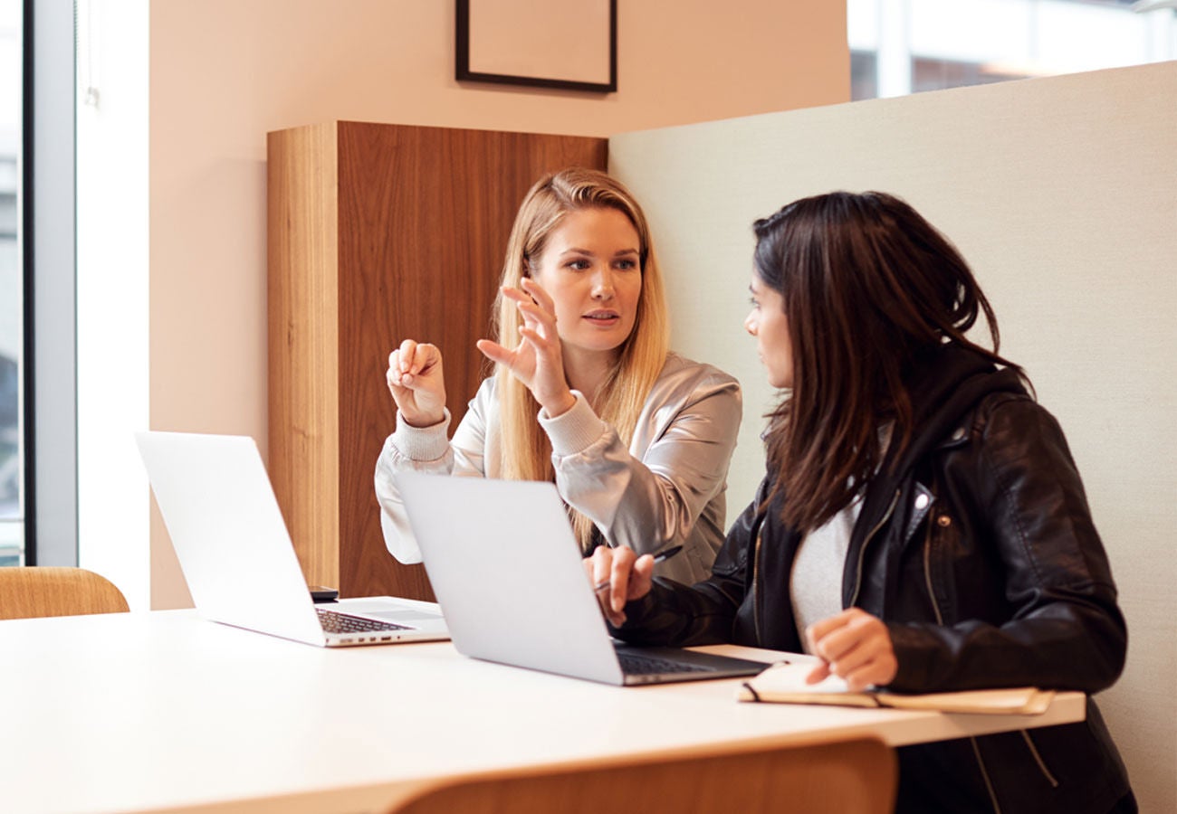 Two Young Businesswomen In Meeting Around Table In Modern Open Plan Workspace