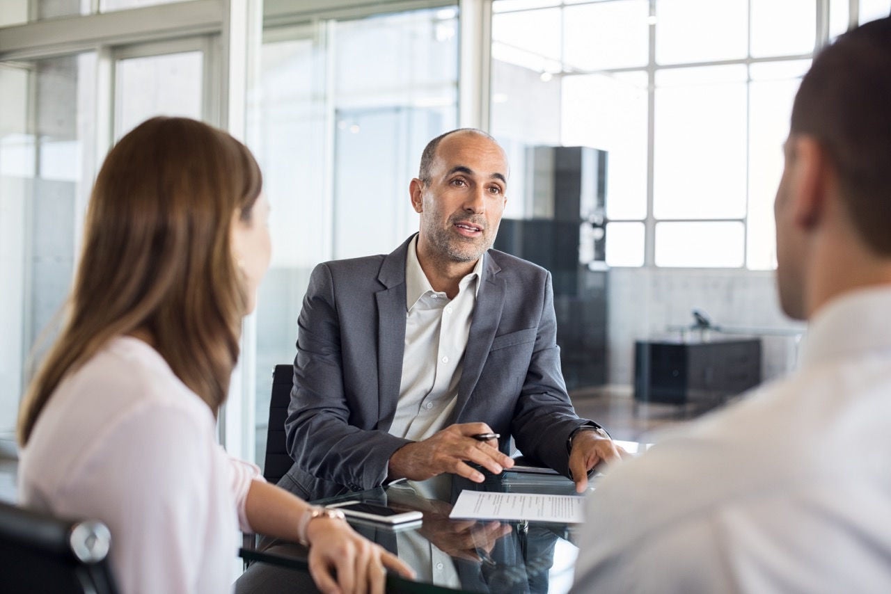 Person presenting a paper to a couple during a meeting in an office