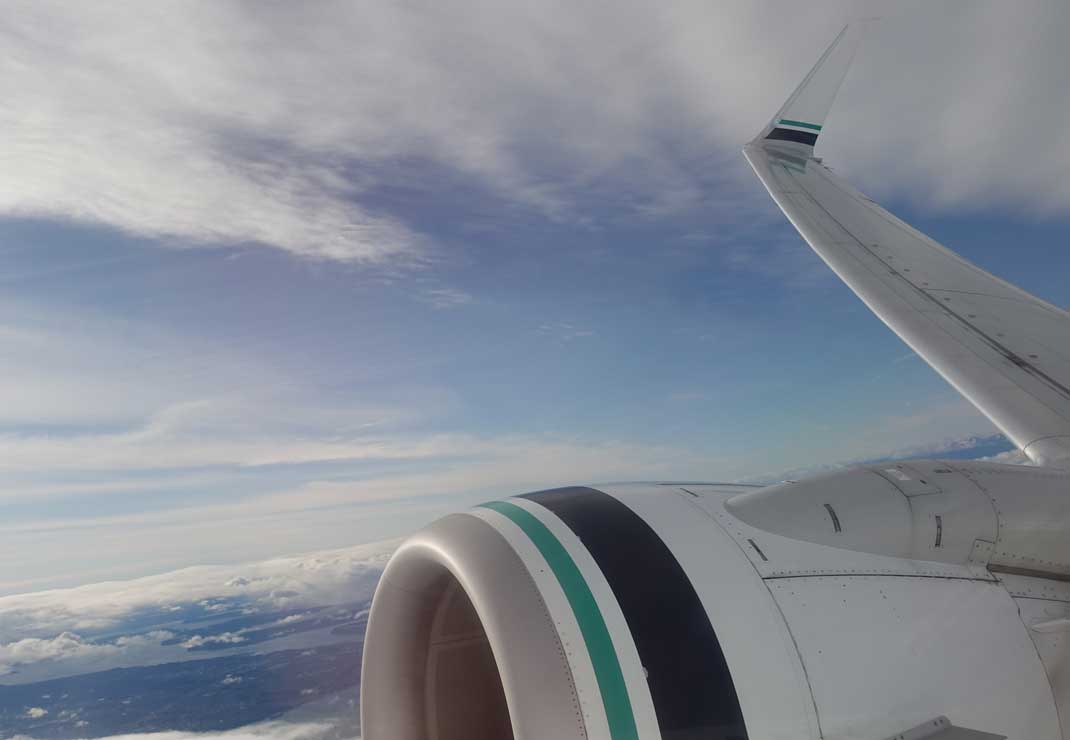 Looking at an airplane window and seeing the blue skies and the turbine from the airplane.