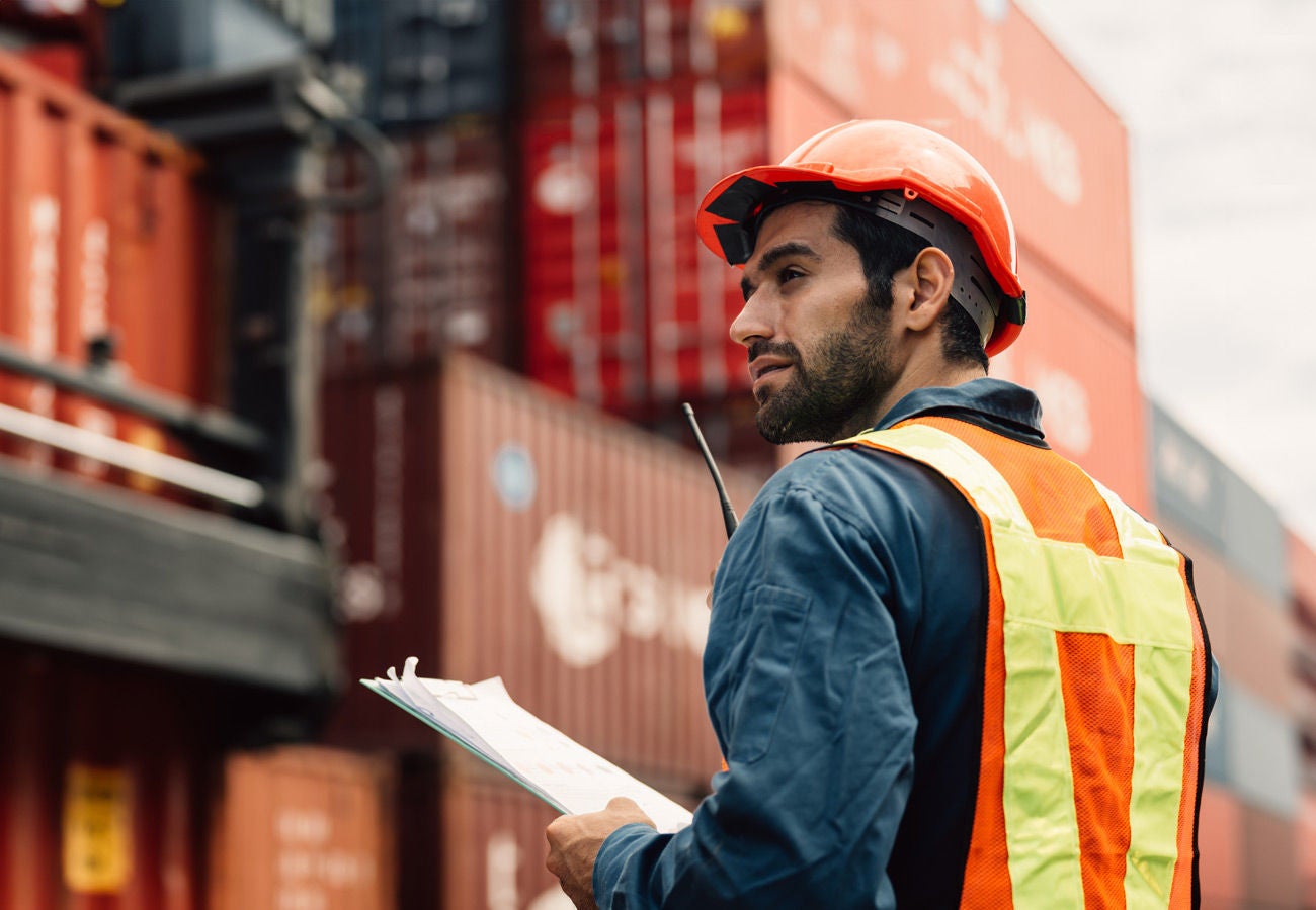 A dock worker manages shipping containers at a seaport.