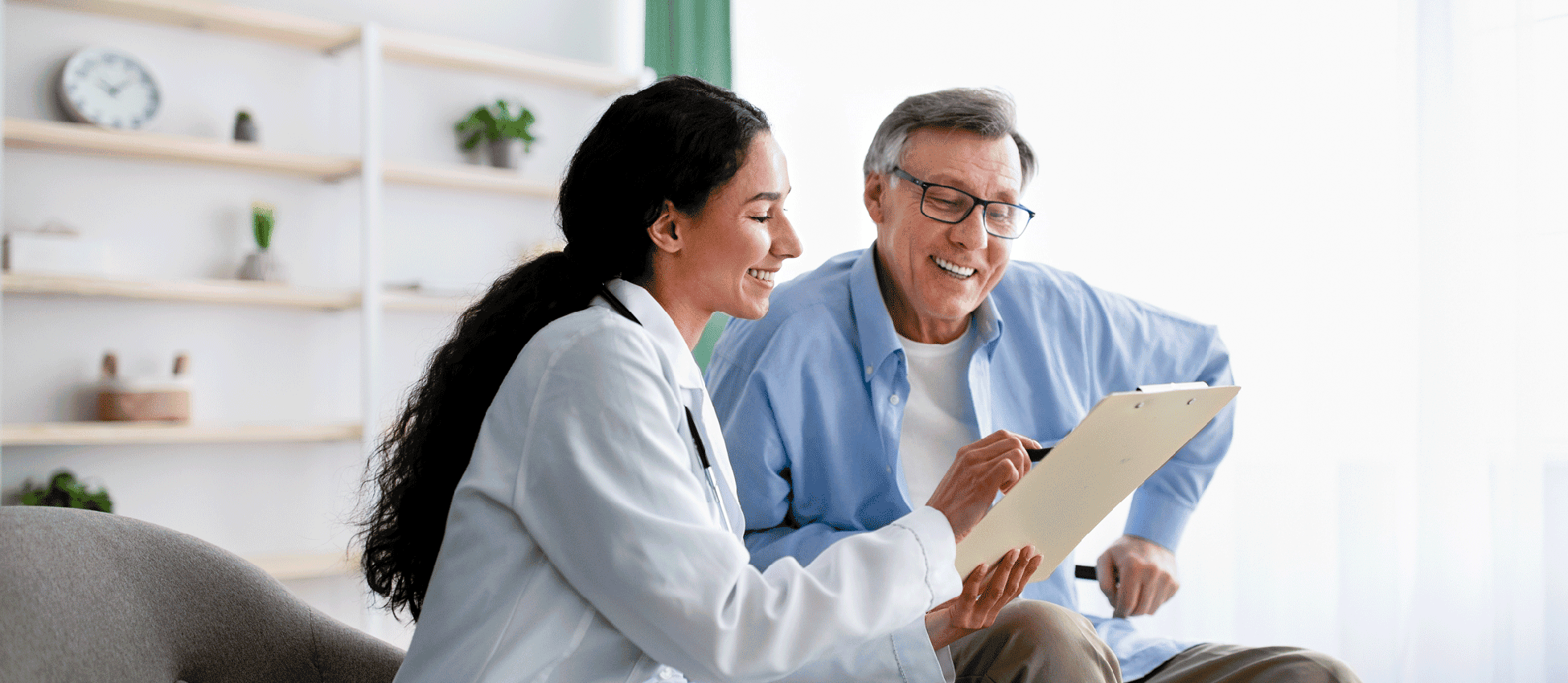 Young doctor asking senior impaired male patient in wheelchair to sign insurance policy at home