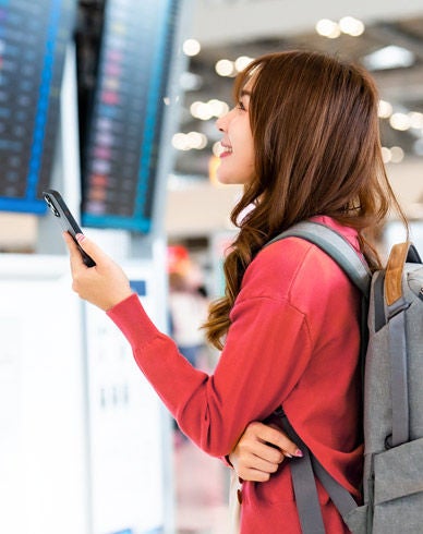 Woman on cell phone looking at departure screen at airport