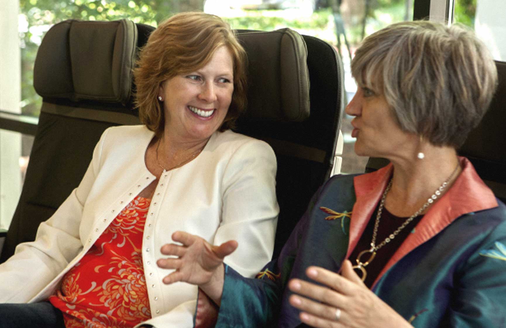 Two women chatting on airplane seats.