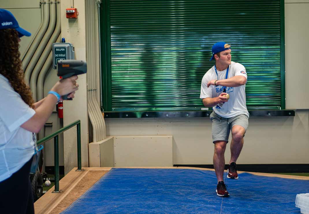 A man practices his pitch with someone measuring its pitch speed. 