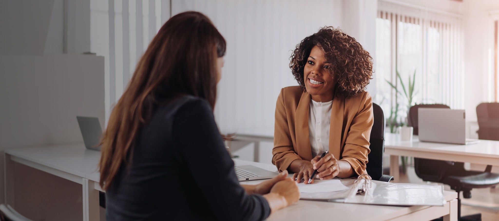 Two women sitting at a desk in an office reviewing papers