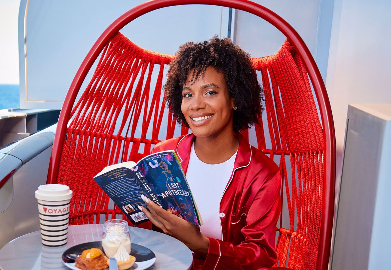 A happy and relazed Virgin Voyages passenger starts their day with breakfast and reading.